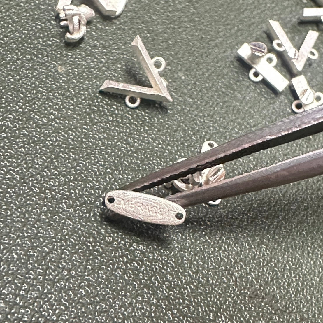 Close-up of silver jewelry components on a textured surface with tweezers.