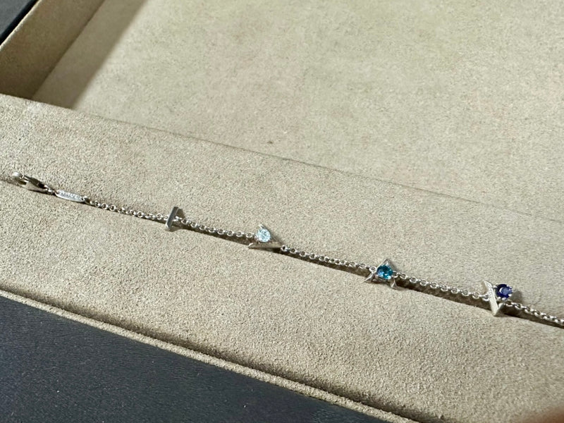 Silver bracelet with "I am greater than my highs and lows" charms and blue gemstones on a beige surface